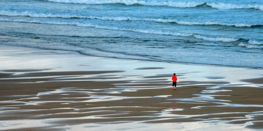 Einsame Person steht am Strand und blickt auf das Meer
